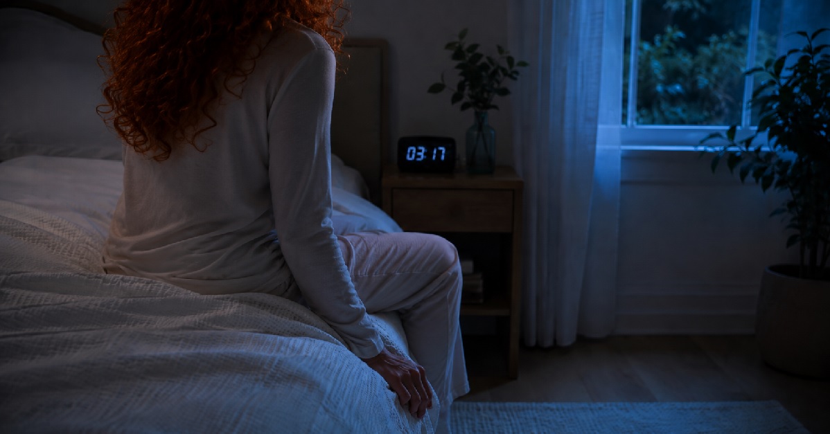 Mulher de costas, sentada na beira da cama durante a madrugada, com relógio mostrando 03:17 ao fundo.